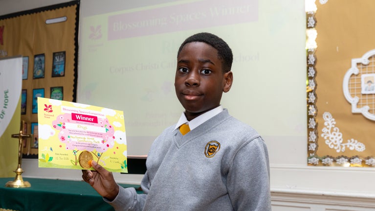 A young child hold a winners certificate for the Blossom Competition